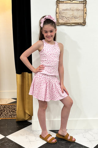Young girl in a pink dress standing in a room with a checkered floor and decorative wall.