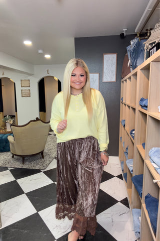 Woman in a yellow top and brown skirt standing in a store with shelves and decor.