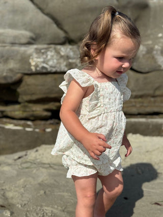 Young child in a white floral dress standing on a rocky surface.