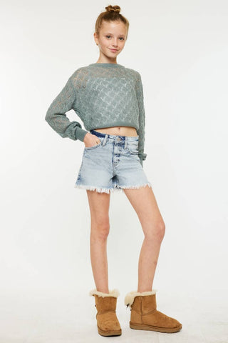 Person wearing a green sweater, denim shorts, and brown boots on a white background