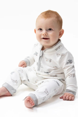 A baby sitting on a white studio background wearing a white long-sleeve zip-up sleeper with a gray and black animal print.