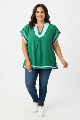 Woman wearing a green top with white trim and blue jeans on a white background