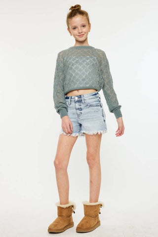 Young girl wearing a green sweater, denim shorts, and brown boots on a white background
