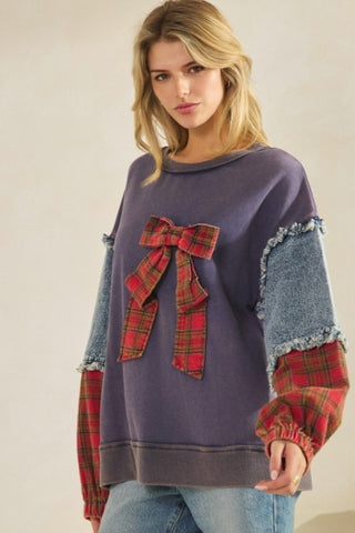 Woman wearing a purple sweater with plaid bow and cuffs on a plain background