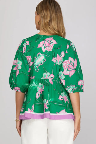 Green floral blouse with pink accents worn by a person on a white background