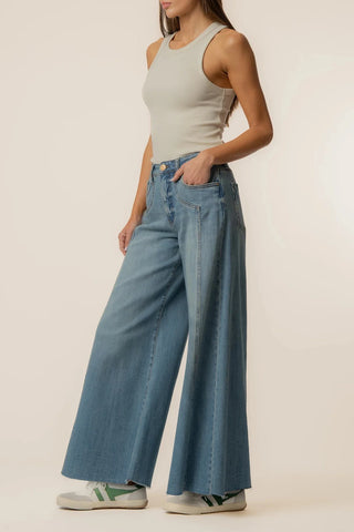 Person wearing a light gray tank top and blue wide-leg jeans on a beige background