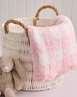 Wicker basket with pink and white striped blanket and plush toy on a light background