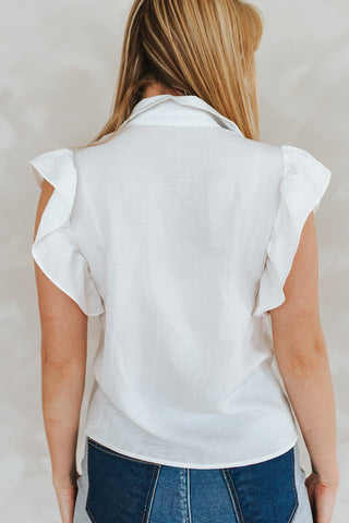 Person wearing a white sleeveless top with ruffled shoulders against a plain background