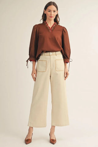 Woman wearing a brown blouse with lace details and beige wide-leg pants on a white background