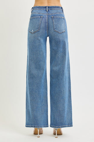 A person shown from the back wearing light blue wide-leg denim jeans with a faded wash and tan heeled sandals, against a plain light gray studio background.