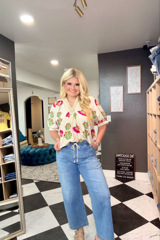 Woman in a floral blouse and blue jeans standing in a room with checkered floor and shelves.