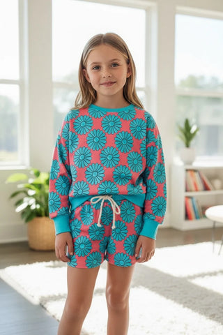 Young girl wearing a colorful patterned outfit in a bright room with large windows.