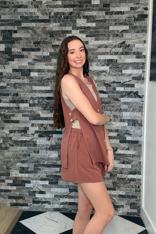 Woman wearing a brown dress standing against a patterned wall.