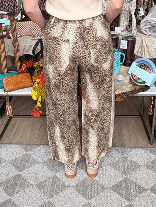 A person wearing wide-leg leopard-print pants, standing in a retail store. The pants feature a brown, beige, and black animal pattern.