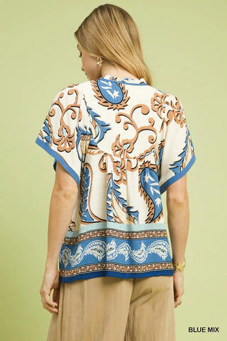 Woman wearing a patterned top with blue, brown, and white design on a light green background