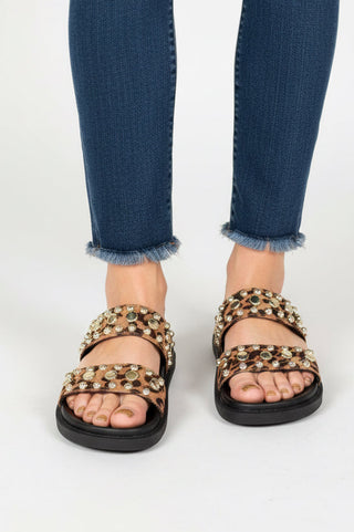 Person wearing embellished sandals with blue jeans on a white background