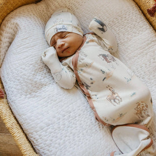 Newborn baby sleeping in a crib with a patterned outfit and hat.