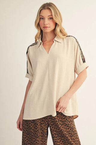 Woman wearing a beige blouse with leopard print accents and leopard print pants on a beige background