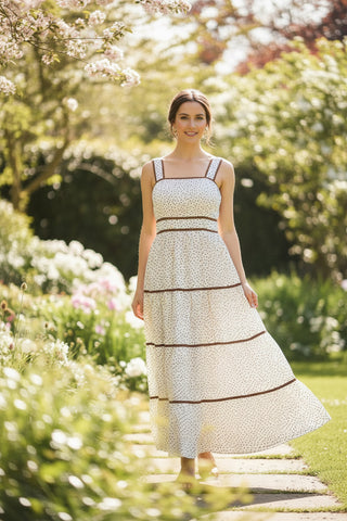 Woman in a white dress with black patterns standing in a garden with greenery and flowers.