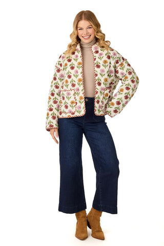 Woman wearing fall floral print quilted jacket, taupe turtleneck, dark wash jeans and camel boots in front of a white background.