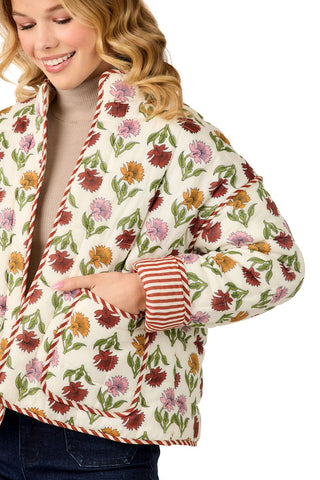 Woman wearing fall floral print quilted jacket, taupe turtleneck, dark wash jeans and camel boots in front of a white background.