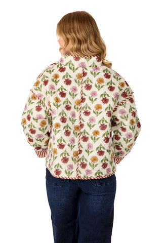 Woman wearing fall floral print quilted jacket, taupe turtleneck, dark wash jeans and camel boots in front of a white background.