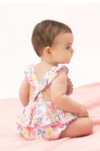 Baby sitting on a pink surface wearing a colorful romper with butterfly design.