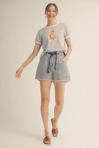 Woman wearing a gray t-shirt with a bear graphic and striped shorts on a beige background