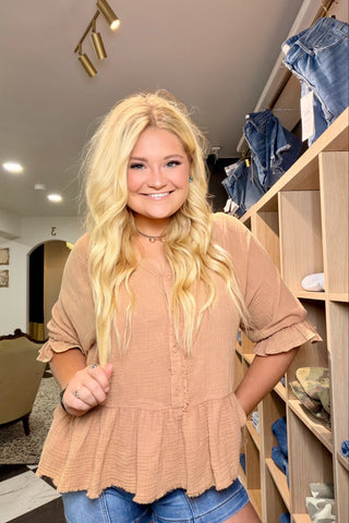 Woman in a beige top and blue jeans standing in a store with shelves in the background