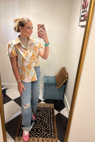 Woman taking a mirror selfie wearing a colorful shirt and jeans in a room with a checkered floor.