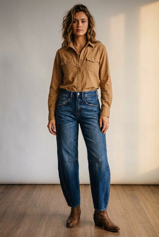 A person wearing loose-fit blue denim jeans with a high waist, faded wash, and raw frayed hems, shown from the waist down on a wooden floor against a light wall.