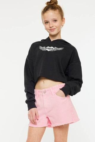 Young girl wearing a black hoodie with a logo and pink shorts on a white background