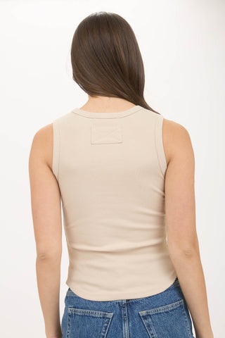 Woman wearing a beige sleeveless top and blue jeans on a white background