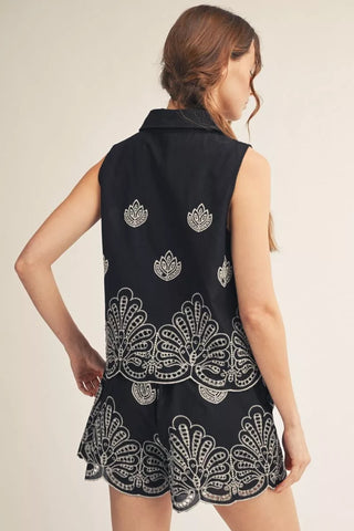 Woman wearing a black sleeveless dress with white floral patterns on a beige background