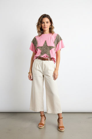 Pink top with leopard print stars held by a hand in a clothing store.