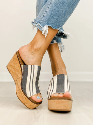 Striped platform sandals with cork wedge sole worn with blue jeans on a neutral background