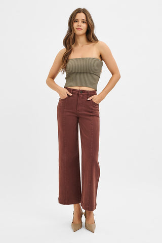A woman modeling a ribbed strapless tube top in olive green and high-waisted wide-leg pants in rust brown, paired with beige heels, against a plain white studio background.