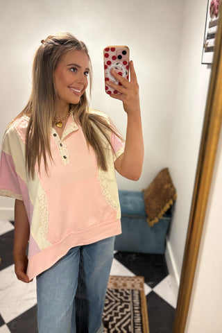 Woman taking a mirror selfie wearing a pink and beige top with lace details.