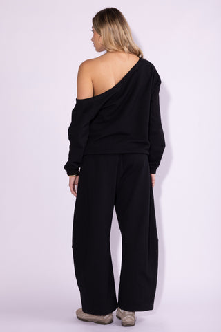 A woman shown from the back wearing a black one-shoulder long-sleeve top and matching wide-leg pants against a plain light background.