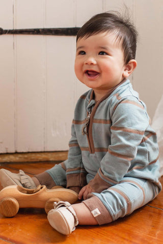 Baby sitting on a wooden floor wearing a striped outfit, smiling.