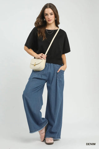 Woman wearing a black top and blue denim pants with a beige handbag on a white background