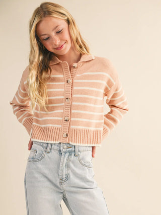 A woman wearing a cropped, long-sleeve knit cardigan with horizontal peach and cream stripes, paired with light-wash jeans, against a solid beige background.
