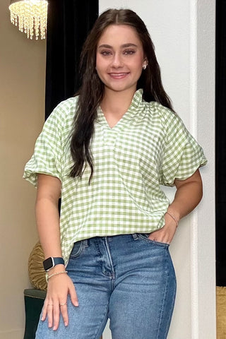 Woman wearing a green checkered shirt and blue jeans indoors.