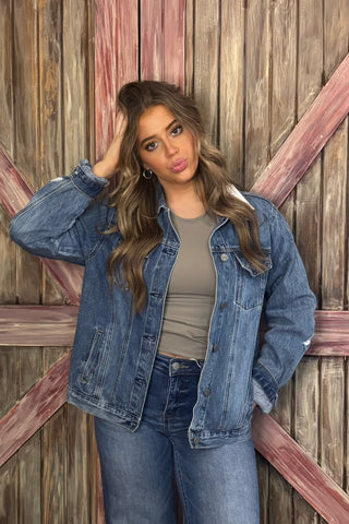 Woman wearing a denim jacket and jeans against a wooden background
