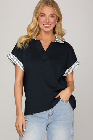 Woman wearing a black top with white trim and light blue jeans on a gray background