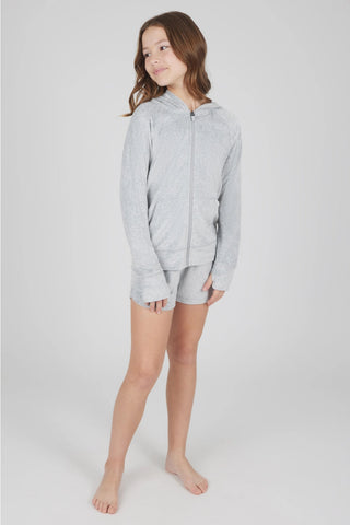 A young girl modeling a light gray heather zip-up hoodie and matching shorts set against a plain light gray studio background.