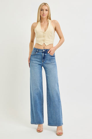 A woman modeling a light beige halter crop top and high-waisted, wide-leg blue denim jeans against a plain white studio background.