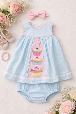 Light blue baby dress with cupcake design and matching bloomers on a light background with flowers and shoes.