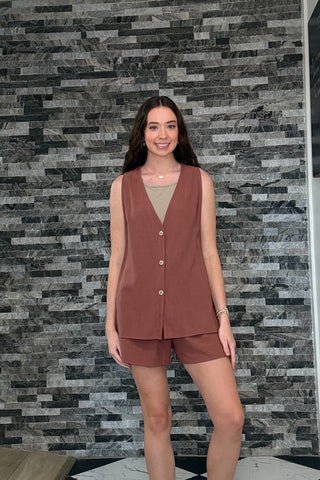 Woman wearing a brown sleeveless top and shorts set against a patterned wall.