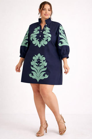 Woman wearing a navy dress with green floral patterns on a white background